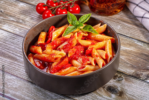 Penne pasta tossed in rich tomato sauce garnished with fresh basil leaves inside round ceramic bowl on rustic wooden table