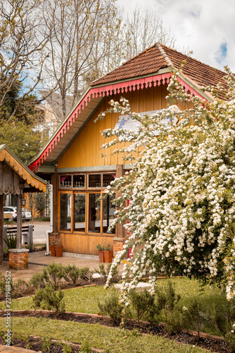 Traditional wooden house with ornate trim, tiled roof, blooming white flowers, and landscaped garden in southern Brazil.