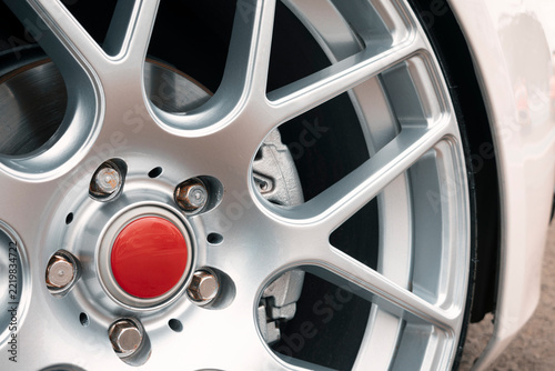Close-up of a silver alloy car wheel with red center cap, rusty lug nuts, brake caliper, and disc.
