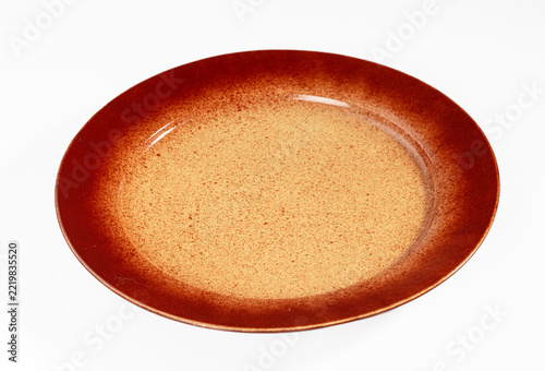 White surface holding empty round ceramic plate featuring speckled brown and orange glaze pattern for kitchenware design