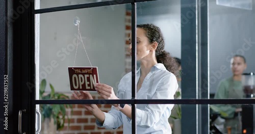 Diverse shop team watching Asian owner opening shop, flipping hanging sign to OPEN, unlocking door