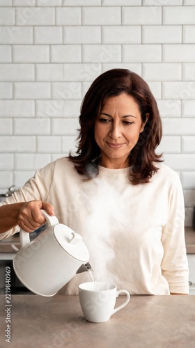 Woman pouring boiling water from kettle into cup