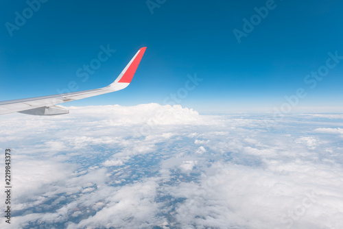 Airplane wing flying high above dense white clouds under a clear blue sky.