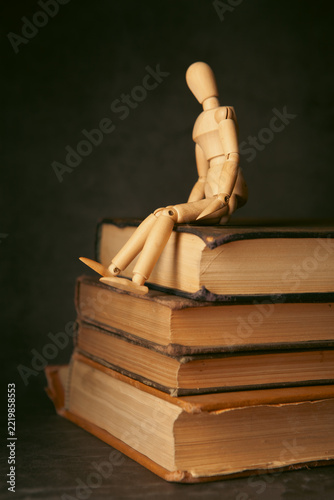 Wooden mannequin sitting on a stack of old books on dark background
