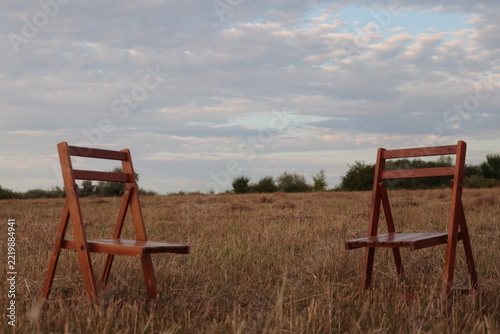 Empty folding wooden chairs in a grassy field.