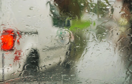 Abstraktes Motiv mit Wassermuster auf Glasscheibe vor fahrendem weißen Kastenwagen mit rotem Rücklicht auf nasser Hauptstraße mit Licht in Dorf bei Regen, Sturm und Kälte am Nachmittag im Herbst