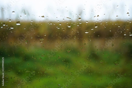 Abstraktes Landschaftspanorama mit Regentropfenmuster vor grüner Wiese, braunem Ackerfeld mit Baumreihe und grau-blauem Himmel auf dem Land bei Regen, Sturm und Nebel am Morgen im Herbst