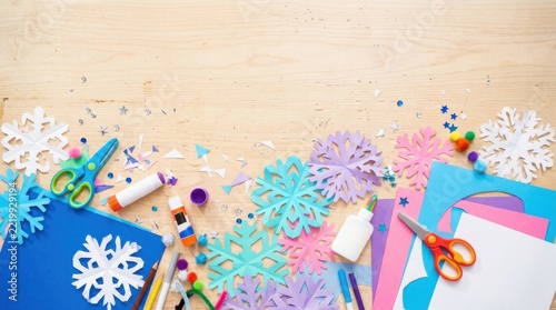 Paper snowflakes and craft supplies on a wooden table for winter holiday decorations and creative DIY art projects
