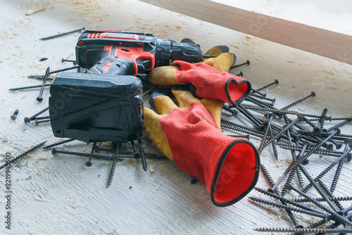 Cordless drill-driver for driving screws and drilling; work gloves; screws for home repairs.