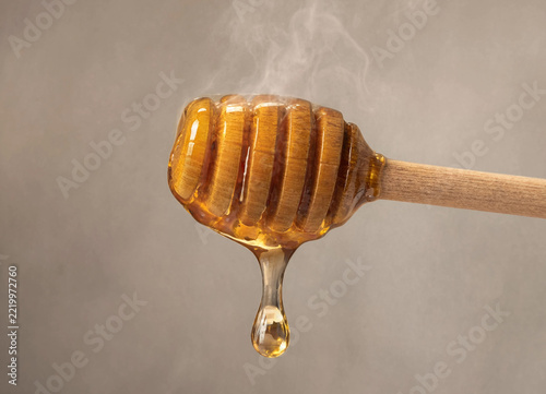 Fresh golden honey dripping from a wooden honey dipper against a neutral background