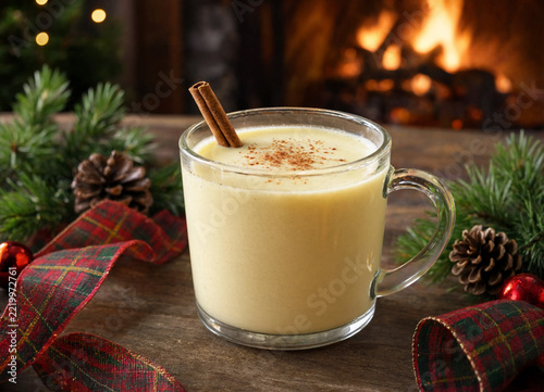 Glass mug filled with creamy eggnog decorated with cinnamon sticks and holiday festive ornaments