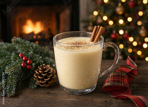 Glass mug of eggnog with cinnamon sticks and nutmeg sitting on wooden table during holiday season
