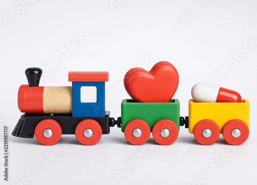 Colorful wooden toy train carrying a red heart shape and medical pill