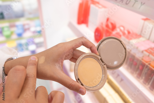 Woman testing foundation shade on skin in beauty store with blurred cosmetic products background and soft lighting