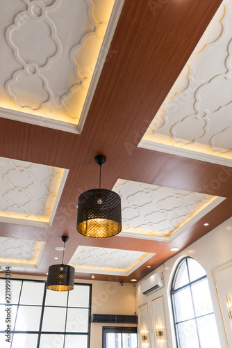 Elegant interior ceiling design with warm wood panels ornate white plaster details and modern pendant lights in a sophisticated space