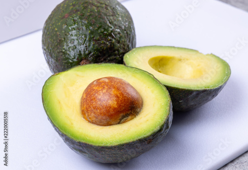 A cut in half avocado showing the brown pit with a whole avocado in the background
