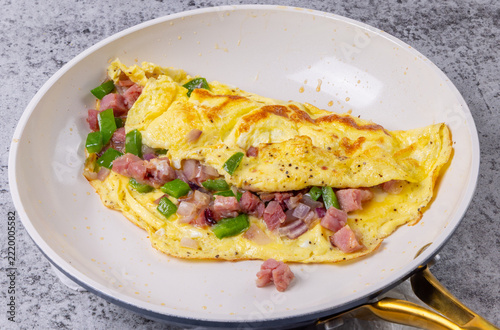 A breakfast Denver omelette with ham, green bell pepper and onion in a white ceramic non stick frying pan
