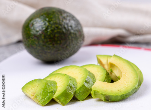 A sliced avocado on a white cutting board with a whole avocado soft focus in the background
