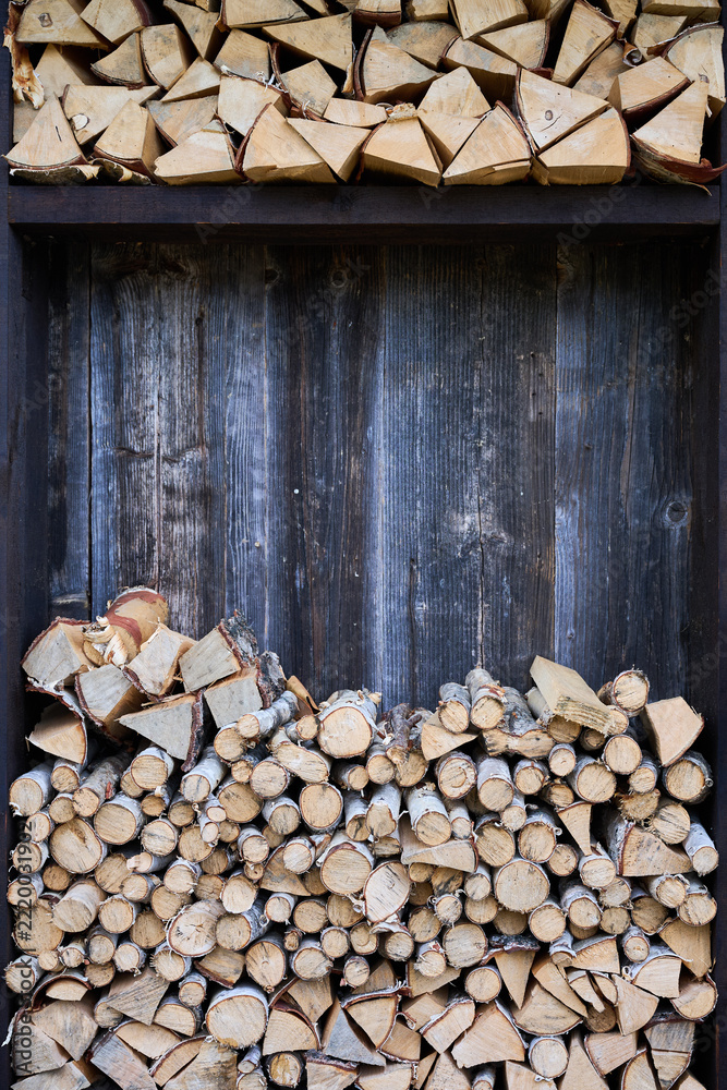 Fototapeta premium Chopped firewood stored in wooden rack against rustic wall. Stacked logs arranged in sections