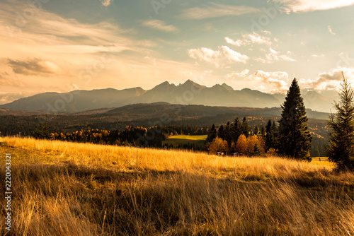 Majestic panoramic view of the Tatra Mountains landscape featuring snow-capped peaks, colorful forests, and picturesque valleys under a dramatic sky. Beautiful scenic nature and wilderness background