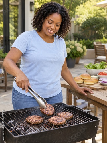 Woman Turning a Burger with Steel Tongs beside a Garden Prep Table