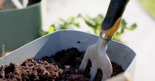 Planter and hand cultivator pressing into soil at sunny patio preparing for transplanting seedlings