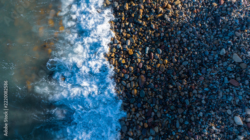 An overhead view of a beach coast in Mexico in the morning, featuring blue water and rocks; a fallen tree trunk lies on the shore, with waves washing over it.