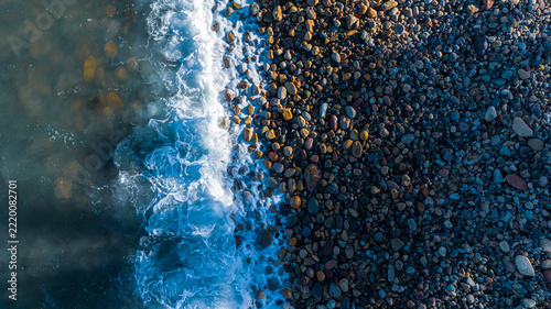 An overhead view of a beach coast in Mexico in the morning, featuring blue water and rocks; a fallen tree trunk lies on the shore, with waves washing over it.