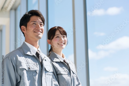 明るい青空の下で作業服の日本人男女2人が未来を見つめる笑顔