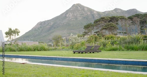 Camera is panning right, revealing two dark wood loungers beside narrow pool, showing shed and peak