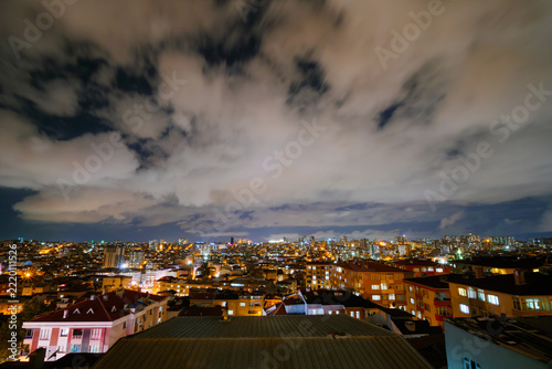 Wide angle view: clouds in the dark sky over typical turkish residential buildings with warm illumination and illuminated windows in Istanbul, Turkey at night - cloudscape, urban and cityscape concept