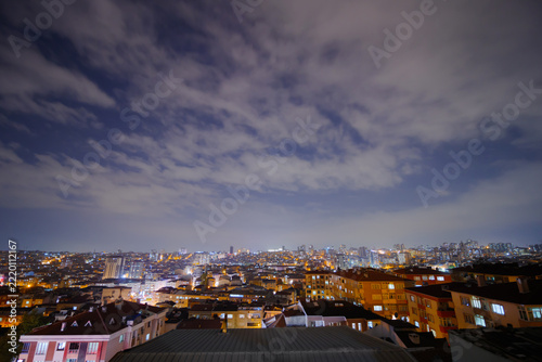 Wide angle view of clouds in the dark sky over cityscape with turkish apartment, residential buildings with warm lighting and illuminated windows in Istanbul, Turkey at night