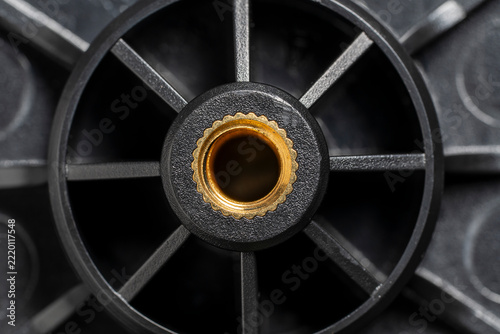 Black plastic wheel detail with brass metal threaded insert. Industrial plastic component with golden brass nut. Mechanical part with radial spokes for engineering, hardware and manufacturing concept