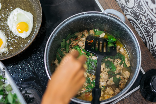 Cooking Thai Pad Kra Pao with chicken and fried eggs in kitchen