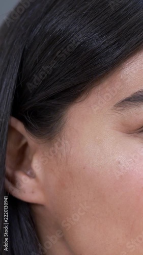 Vertical video: Framing adult Asian woman making tiny facial movements in studio, showing ear stud