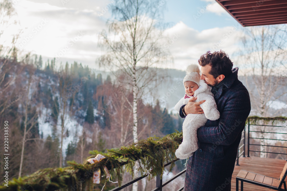 Fototapeta premium Dad and his baby girl enjoy snowy mountain landscape from hotel terrace. Family spends weekend in rented house for winter holidays