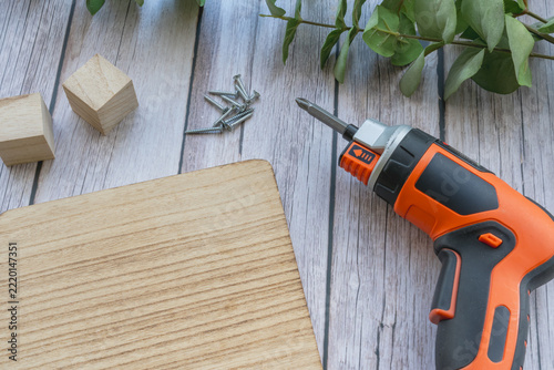 Fotografie An electric cordless screwdriver with screws and wooden board on wood background with copy space for DIY concept
