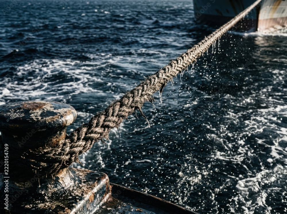 Fototapeta premium Weathered rope mooring line on bollard above dark harbor water