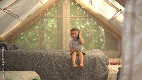 Cute Little Boy Sitting in Inflatable Play Tent on Bed Talking on Mobile Phone