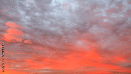 Vibrant sunset colors fill the sky. Deep reds glow near horizon. Pink clouds float above gray tones. Soft light bathes scene. Ideal for travel or relaxation themes
