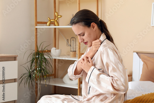Skin allergy and irritation, woman scratching itchy arm in bedroom at home wi...