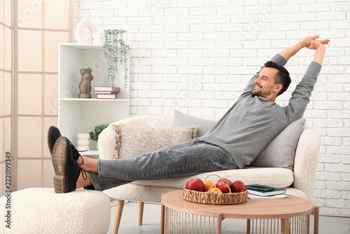 Work-life balance and relaxation, man stretching on a sofa at home after a lo...