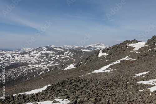 Panoramic view of rugged rocky slopes and snow patches on Mount Konzhakovsky Kamen under a clear blue sky in Sverdlovsk Oblast, Russia during bright spring season