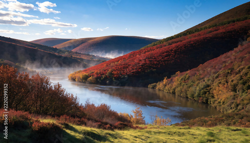 Vibrant autumn forest scene with winding river and misty hills for