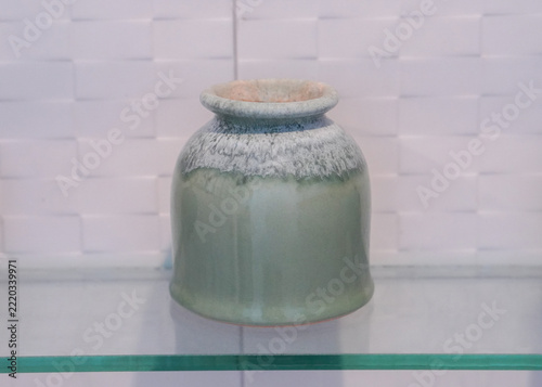 front view antique green and white ceramic pot, on a glass shelf, white ceramic wall background, object, decor, fashion, copy space