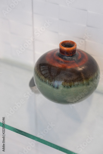 top view antique brown and green small ceramic vase, on a glass shelf, white ceramic wall background, object, decor, fashion, copy space