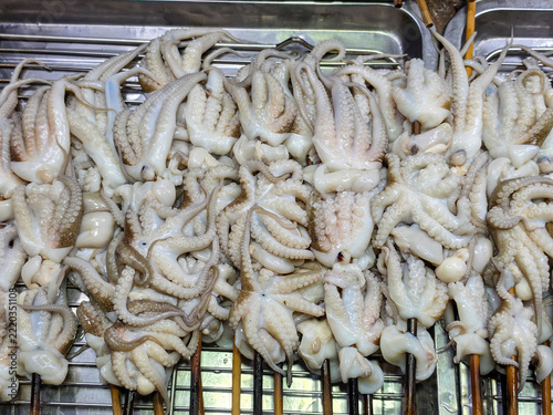 A dense pile of small pale octopus tentacles skewered on wooden sticks, heaped inside a stainless steel tray.