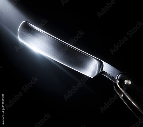 Straight razor blade catching sharp beam of light on dark background