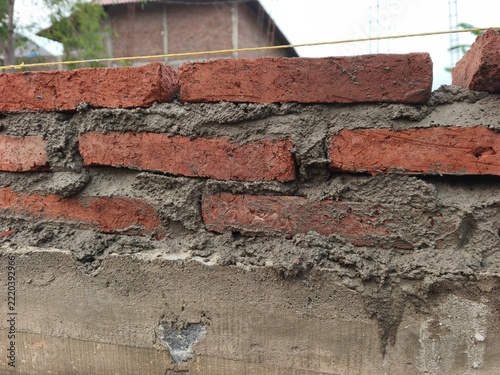 Red brick masonry wall laying on concrete foundation with cement mortar at building construction site, perfect for house structure progress, civil engineering, and masonry texture photo