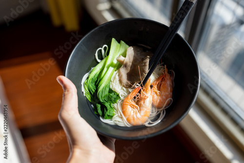 Hand Holding Bowl of Shrimp Noodle Soup with Green Vegetables